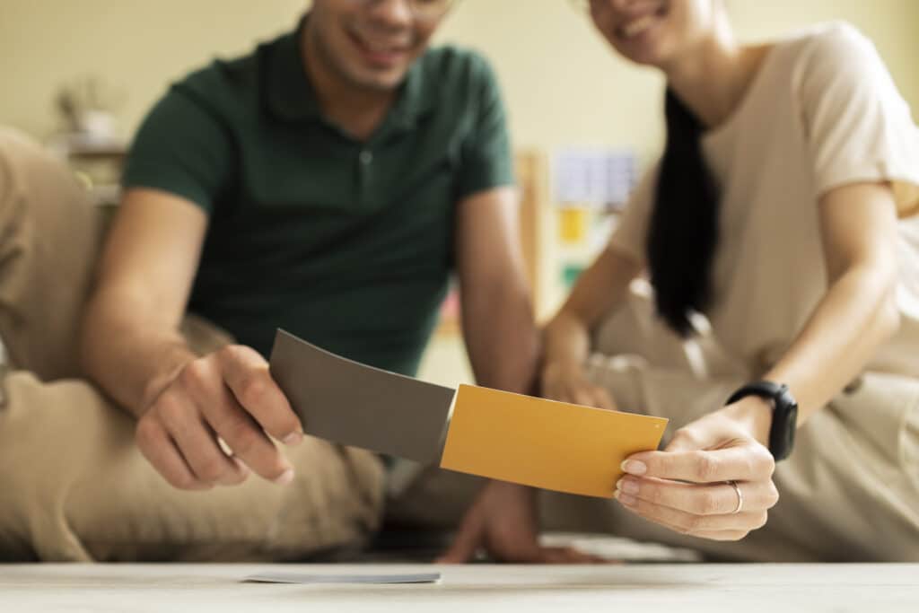 Un couple sourit en comparant des échantillons de peinture de couleur grise et jaune pour leur projet de décoration.