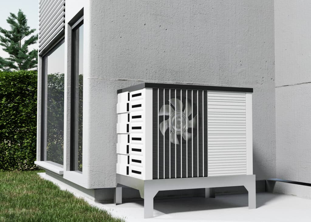 Une unité extérieure de pompe à chaleur installée sur un support métallique contre le mur extérieur d'une maison moderne, près d'une fenêtre et d'une haie.