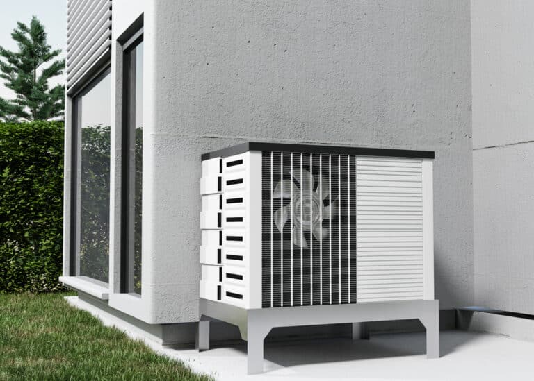 Une unité extérieure de pompe à chaleur installée sur un support métallique contre le mur extérieur d'une maison moderne, près d'une fenêtre et d'une haie.