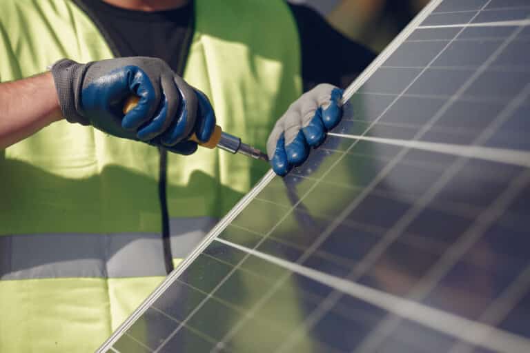 Un technicien portant un gilet de haute visibilité et des gants de protection utilise un tournevis pour installer ou réparer un panneau solaire.